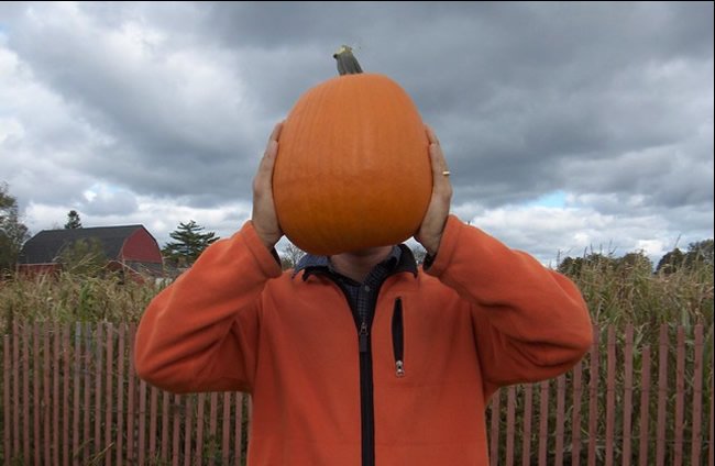 Man in an orange jacket holding a pumpkin in front of his face